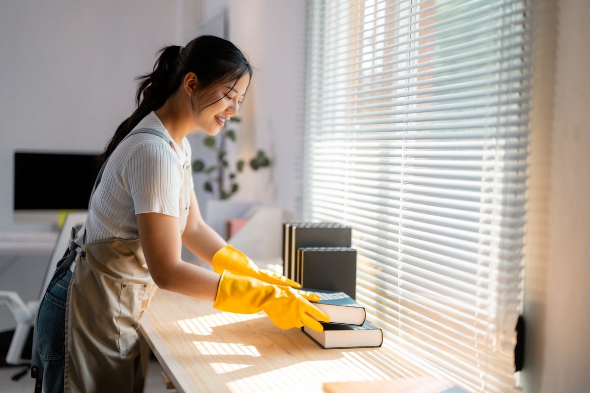 Cheerful housekeeper cleaning a wooden table while wearing yellow gloves